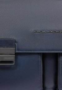 Marineblauwe leren tas met een gestructureerd oppervlak, zwart metalen sluiting, geperst logo en een gestructureerd ontwerp met meerdere compartimenten.