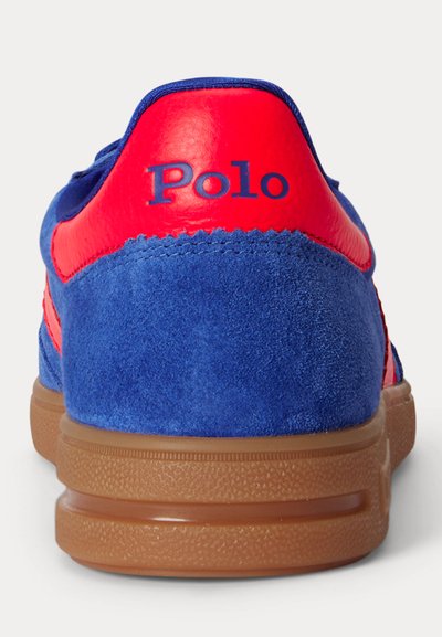 Μπλε σουέτ αθλητικό παπούτσι με κόκκινη δερμάτινη ταμπέλα στη φτέρνα, καφέ λαστιχένια σόλα και το λογότυπο "Polo" τυπωμένο στην ταμπέλα της φτέρνας με μπλε γράμματα.