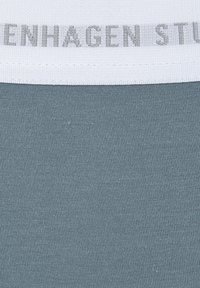Grauer Stoff mit einer feinen gerippten Textur. Weißer elastischer Taillenbund mit einem dezenten grauen Logo-Print. Nahaufnahme, die auf Material und Design fokussiert.