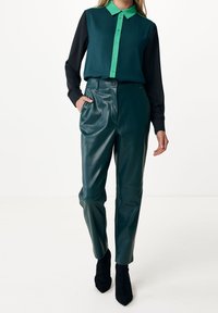 Teal and black two-tone blouse with a button-down design; paired with high-waisted, glossy teal leather trousers and black stiletto boots.