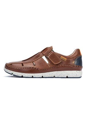 Zapato marrón de piel sin cordones con agujeros de ventilación, tacón oscuro en contraste y suela texturizada salpicada de blanco. Detalles de costura visibles.