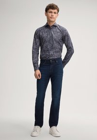 Langärmliges Hemd in Marineblau mit Paisleymuster, kombiniert mit dunkelblauen Jeans und weißen Sneakers. Das Hemd zeichnet sich durch ein komplexes Muster und einen Knopfverschluss aus.