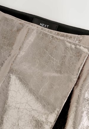 Metallisch silberner Rock mit einer zerknitterten Textur, ausgestattet mit einem schwarzen Bund und einem dezenten Logoetikett innen. Glatte, reflektierende Oberfläche.