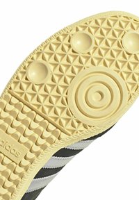 Semelle de sneaker noire et grise avec un fond en caoutchouc beige texturé présentant des motifs triangulaires et des détails circulaires près du centre.