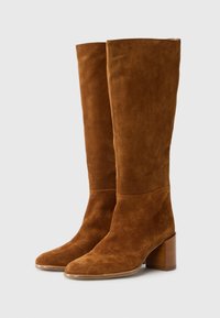 Bottes en suède marron jusqu'au genou avec un bout pointu et un talon en bois massif, dotées d'une texture lisse et d'un design minimaliste.