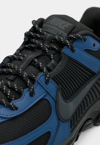 Close-up de um sapatilhas Nike Air VaporMax preto e azul com atacadores pretos refletivos e um tecido em malha texturizado.