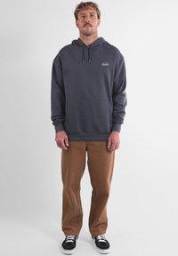 Hoodie marine avec une poche avant, capuche à cordon et accent logo. Assorti avec un pantalon beige et des baskets noires. Texture lisse, coupe décontractée.