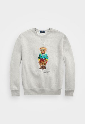 Jasnoszara bluza z kolorowym misiem Polo Bear w okularach przeciwsłonecznych, zielonej kurtce, brązowych spodniach i butach, podpisana przez Ralph Lauren poniżej.