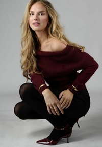 Burgundy off-shoulder tröja med ribbad textur, ihop med svarta tights och högklackade skor i lackläder. Guld smycken som accenter.
