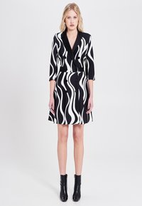 Schwarz-weißes Kleid mit Wellenmuster, Dreiviertelärmel, doppelt geknöpftem Design und großen Knöpfen, kombiniert mit schwarzen Ankle Boots.