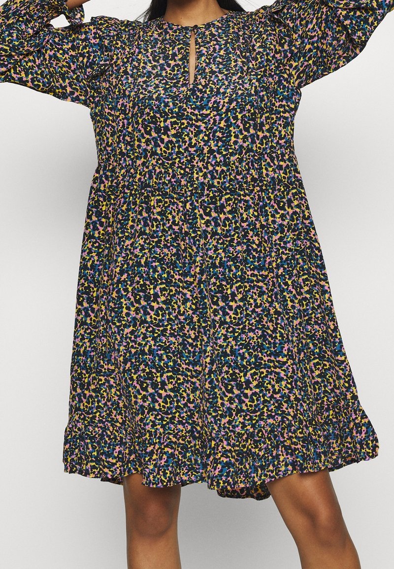 Femme portant une robe à manches longues imprimée d'un motif floral multicolore avec un décolleté en trou de serrure et une taille froncée, debout les bras levés.