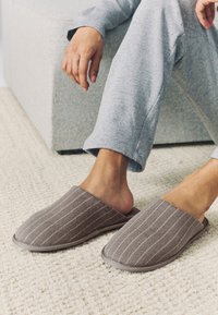 Chaussons en tissu gris à motif rayé, à dos ouvert et bout arrondi. Les chaussons ont une texture douce et une semelle flexible.