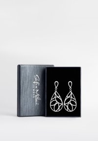 Silverdropörhängen med en intrikat öppen design, presenterade i en svart sammetklädd låda med en slank silveryta.