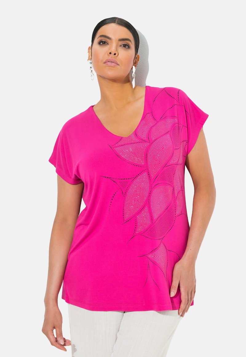 Růžové tričko s V-výstřihem a krátkými rukávy, s květinovým vzorem z malých kamínků na jedné straně. Měkká tkanina s volným střihem.
