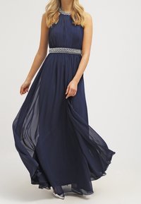 Marin chiffong maxi klänning med plisserad bodice, rund halsringning och dekorerad midja. Flödande kjol som förstärker rörelse och elegans.