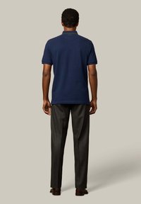 Granatowa koszulka polo z wykrojem kołnierza, krótkimi rękawami i prostym dołem, zestawiona z ciemnoszarymi dopasowanymi spodniami i brązowymi butami.