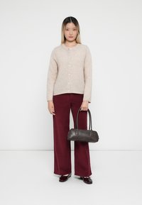 Beige gombos kardigán, széles bordó nadrág és sötét bőrtáska; elegáns dizájn sima textúrával és finom színkontraszttal.