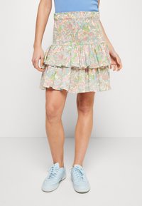 Jupe à volants à motif floral avec taille froncée, présentant des couleurs pastel de rose, vert et bleu. Associée à des baskets bleu clair.