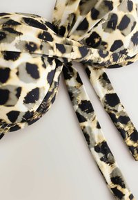 Haut de bikini imprimé léopard avec des coques rembourrées et de longues lanières sur un fond clair.