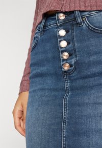 Denim skirt with a high waist, featuring five rose gold buttons along the front. The fabric is medium wash with a smooth, slightly textured surface.
