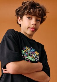 Black short-sleeve t-shirt featuring a colorful graphic print with various animal motifs. Fabric appears soft, with a relaxed fit.