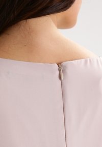 Robe rose clair avec une texture lisse, un large décolleté et une fermeture éclair au dos avec un petit onglet de tirage.