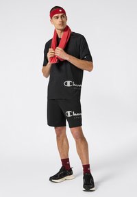 Czarny strój sportowy składający się z koszulki z krótkim rękawem i szortów, oba z białym logo "Champion". Czerwona ręcznik na szyi, czarne tenisówki.