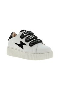 Witte sneaker met zwarte gestructureerde klittenbandsluitingen, voorzien van een zwart bliksemschichtontwerp en een gestructureerde witte rubberen zool.