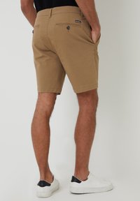 Shorts kaki à coupe slim, avec poches avant et arrière, et accents en bouton ; associés à des baskets blanches avec un onglet de talon noir.
