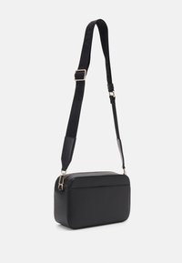 Black crossbody bag made of textured material with a rectangular shape. Features a detachable strap and gold-tone zippers.