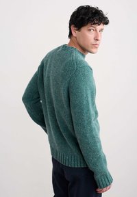 Zeleni pleteni pulover s teksturiranim nitima, rebrastim manžetama i rubom, okruglim izrezom, s suptilnim spektrima kroz tkaninu.