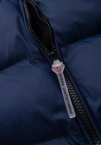 Giacca imbottita blu navy con una ripresa ravvicinata di una cerniera, che mette in mostra un cursore testurizzato con logo e una fodera nera a contrasto.