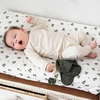 Beige baby body, hvid skiftepude med blomsterprint, grøn sut og klude serviet lagt ved siden af. Træoverflade nedenunder.