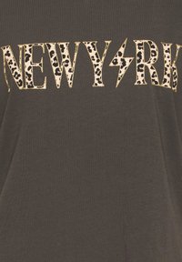 Ciemny materiał z napisem "NEW YORK" w deseniu panterki i złotą obwódką, z błyskawicą zastępującą literę "O".