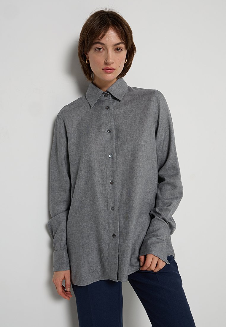 Graues Hemd mit Knopfleiste, Kragen, langen Ärmeln und dunklen Knöpfen. Aus einem strukturierten, gewebten Stoff gefertigt, fällt es locker über einer dunkelblauen Hose.
