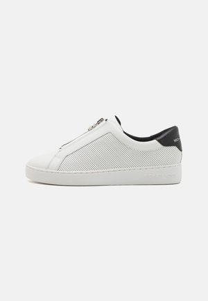 Valkoinen matala sneaker rei'itetyillä sivuilla, musta kantakotelo, vetoketjusuljenta ja paksu pohja, pohjassa kohokuvioitu brändin nimi.