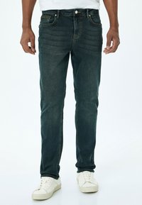 Jeans de mezclilla azul oscuro con un corte recto, que presentan un sutil desvanecimiento, diseño de cinco bolsillos y costuras en contraste, combinados con zapatillas blancas.