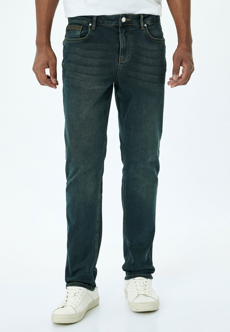 Jeans de mezclilla azul oscuro con un corte recto, que presentan un sutil desvanecimiento, diseño de cinco bolsillos y costuras en contraste, combinados con zapatillas blancas.