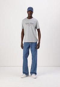 Grå bomulds t-shirt med "Tommy Hilfiger" logo, parret med lyseblå løstsiddende jeans og hvide sneakers. En blå kasket fuldender looket.