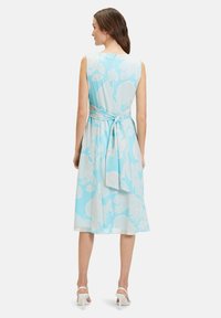 Ein ärmelloses, hellblaues Kleid mit weißen Blumenmustern, tailliert mit einem Bindeband und mit einem knielangen, fließenden Schnitt.