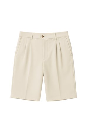 Mann trägt beige knielange Shorts, weiße Socken mit schwarzem Text und braune Velours-Schnürschuhe vor einfarbigem Hintergrund.