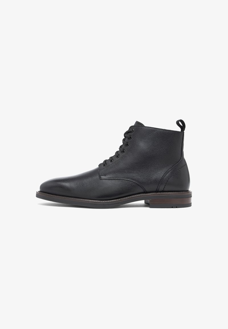 Bottine en cuir noir avec fermeture à lacets devant, bout arrondi, languette au talon et semelle basse marron empilée.