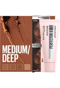 Maybelline 4-in-1 Perfecting Makeup nella tonalità Medio/Scuro, con un tubo rosa, una texture liscia e campioni di colore su uno sfondo marrone.
