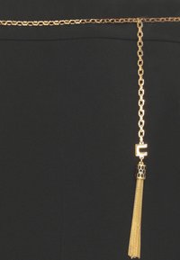 Cintura in catena d'oro con dettagli esagonali e una frangia, su uno sfondo nero, che enfatizza il contrasto di colore e texture.