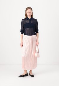 Marineblå, gjennomsiktig strikket polo skjorte med krage, kombinert med en plisserte, lys rosa midiskjørt. Svart leiligheter og en liten rosa håndveske fullfører antrekket.