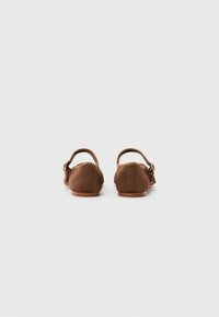 Brown fabric shoes with rounded backs and adjustable straps. Textured surface, flat rubber sole, and subtle stitching details on the sides.