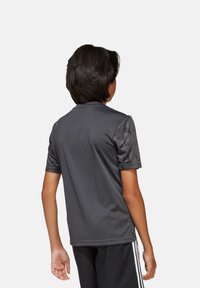 Dunkelgraues Sportshirt mit kurzen Ärmeln, das ein strukturiertes Muster an den Schultern aufweist, aus leichtem, feuchtigkeitsableitendem Material gefertigt.