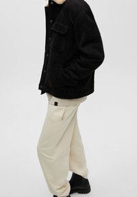 Sort faux suede jakke med en beige shearling krave, enkelt brystlomme, parret med elfenbensfarvede sweats og sorte ankelstøvler.