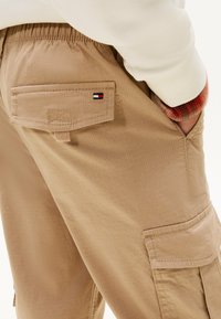 Lichtbruine cargobroek van gestructureerde stof, met een achterzak met gestikte details en een logo-label. Elastische tailleband voor comfort.