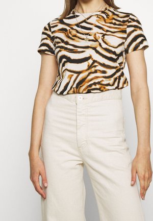 Vrouw die een korte mouw tijgerprintshirt draagt, gestopt in een high-waisted witte broek, geaccentueerd met een ronde hangersketting.